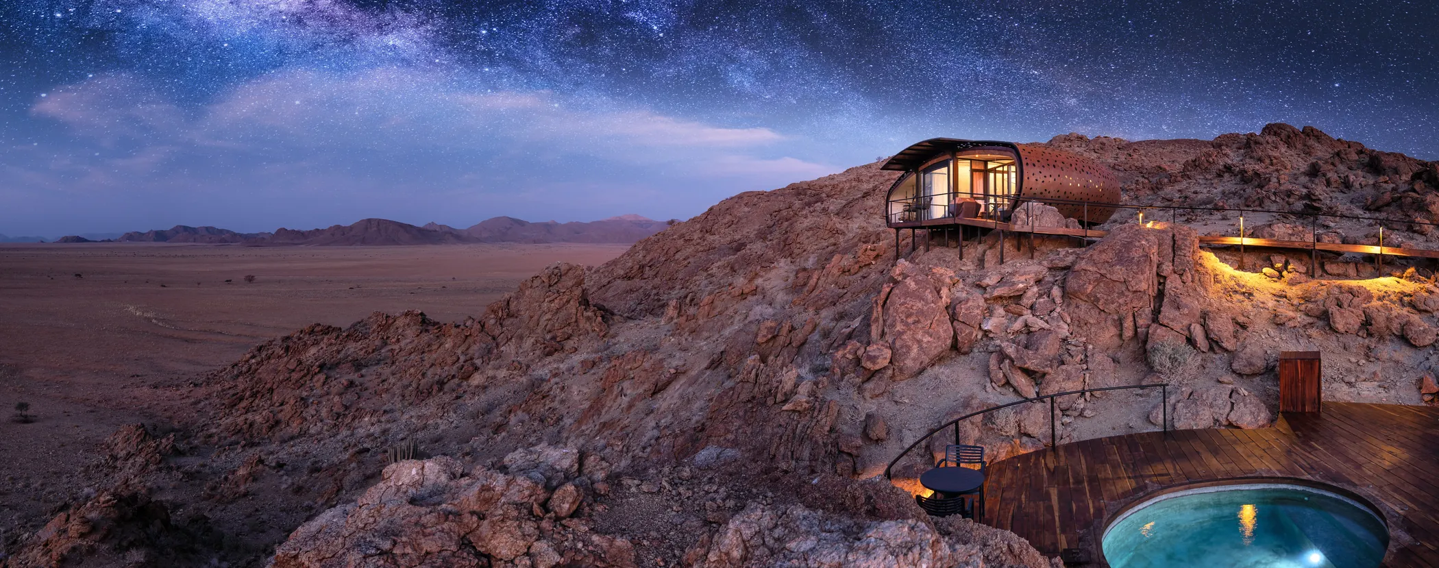 A lit glass pod on a rock ridge under the Milky Way at The Desert Whisper